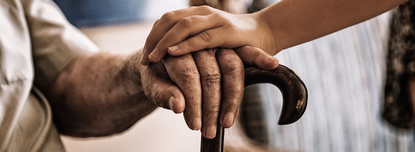 Child’s hand resting on an older adult’s hand holding a cane